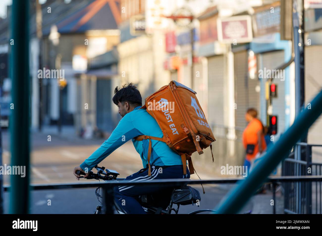 Un pilota di consegna della bici di Just Eat con un grande zaino arancione con il logo Just Eat cicli lungo una strada a Southend on Sea, Essex Foto Stock