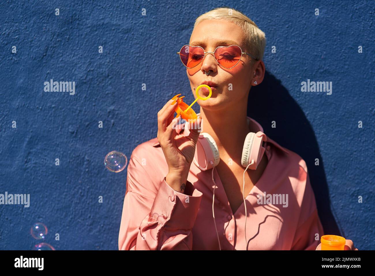 Non lasciate mai che qualcuno scoppii la vostra bolla. Una giovane donna attraente che si trova solo contro una parete blu e soffia bolle all'aperto. Foto Stock