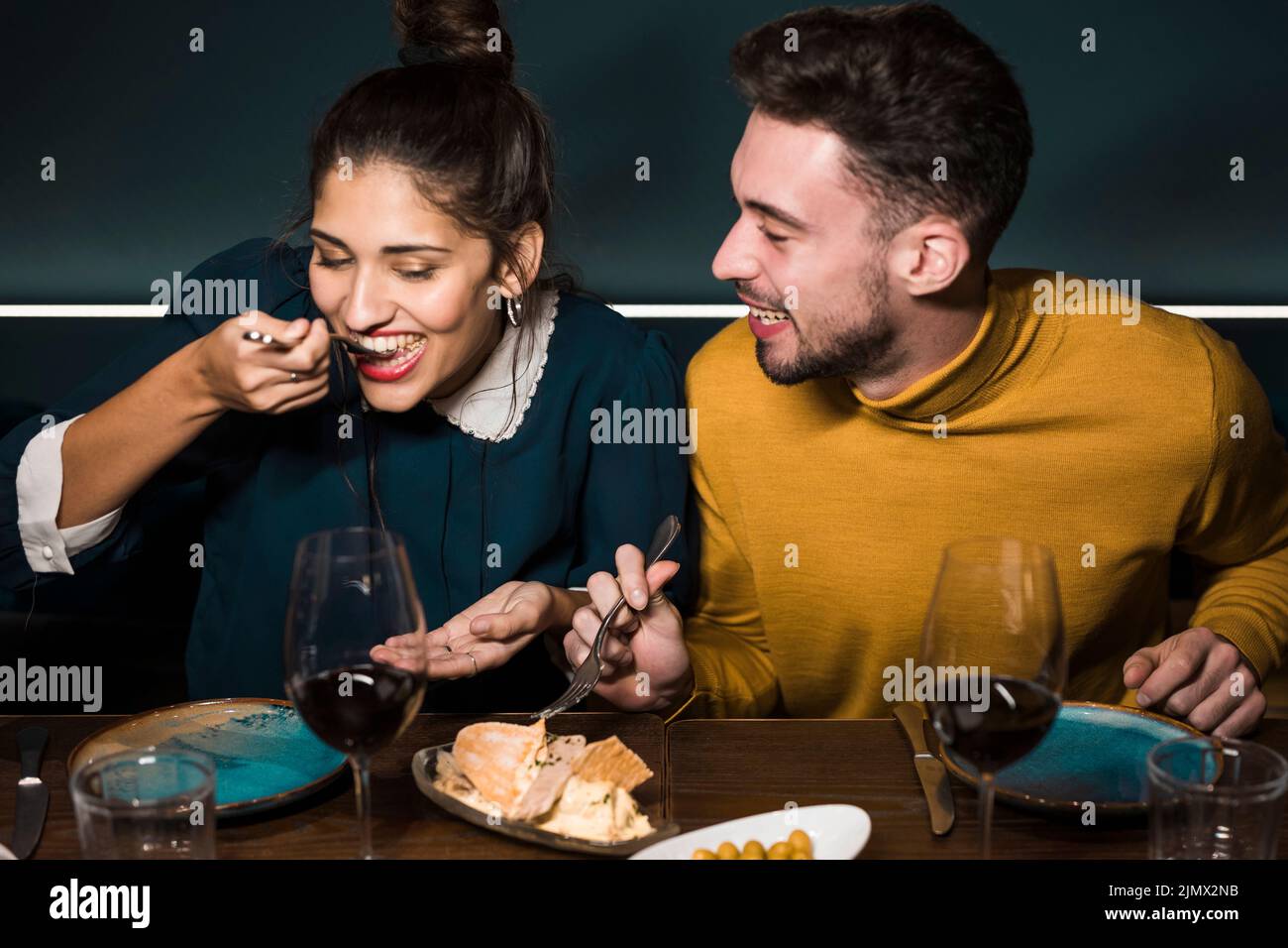 Giovane uomo sorridente che guarda donna con forchette degustazione formaggio tavolo ristorante Foto Stock
