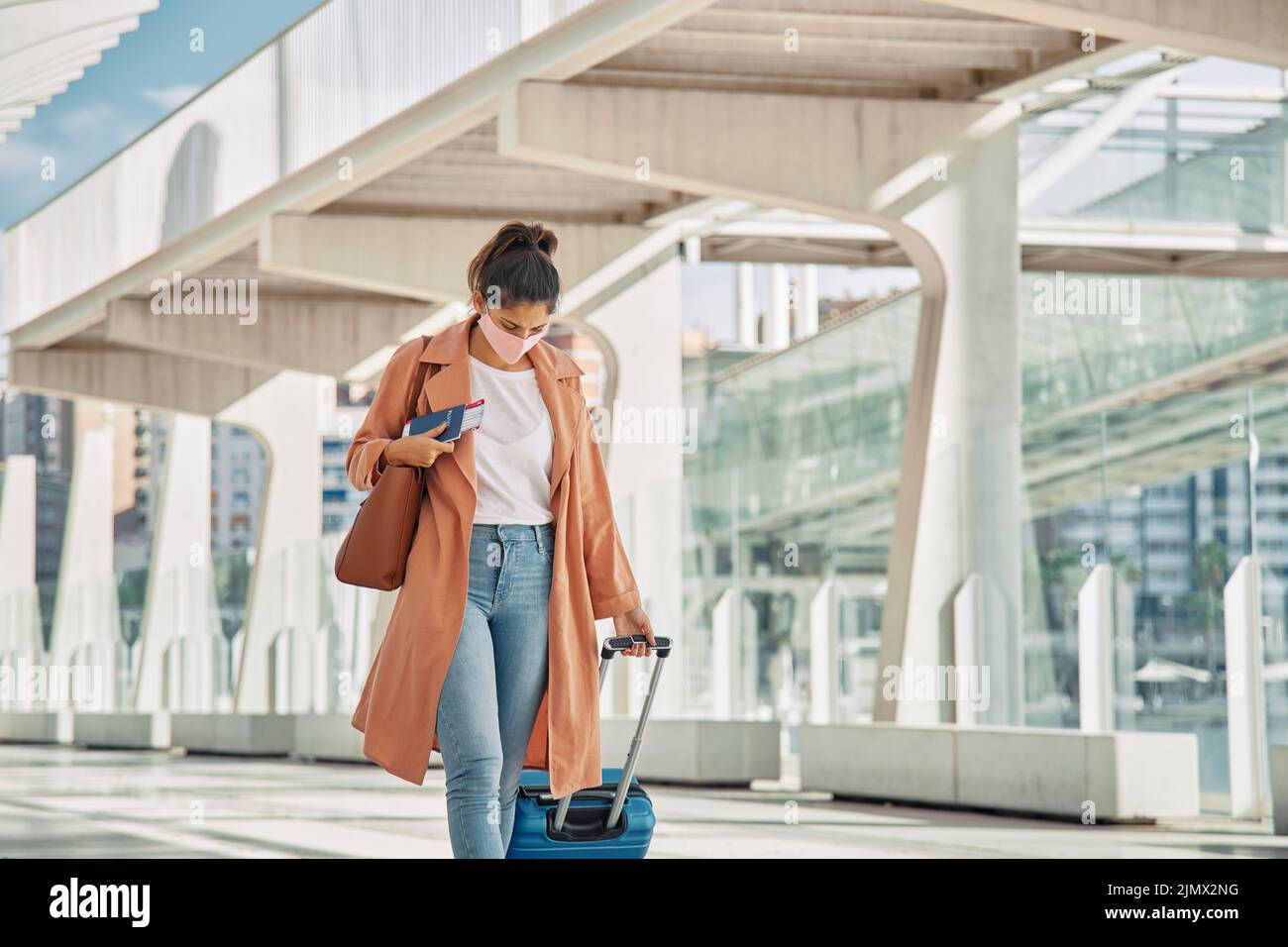 Donna con maschera medica a piedi con il suo aeroporto bagagli durante la pandemia Foto Stock