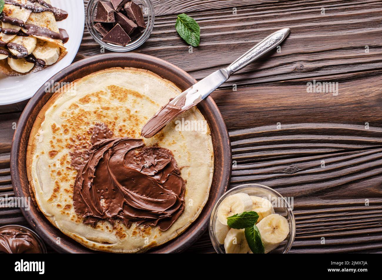 Piatto francese laici crepes con salsa di cioccolato e banana in argilla ciotola di legno sul tavolo da cucina Foto Stock