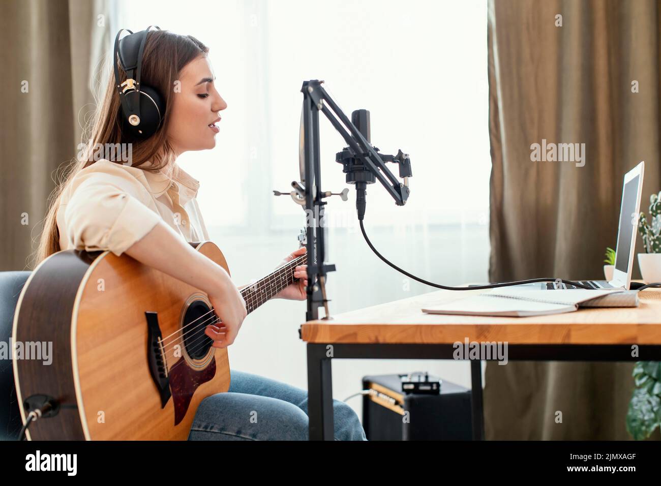 Musicista femminile che registra la canzone a casa mentre suona la chitarra acustica Foto Stock