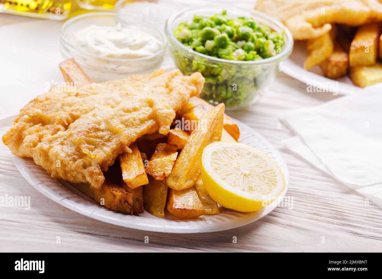 Britannico tradizionale cibo di strada pesce e patatine con salsa tartara e fiacco piselli sul piatto di carta Foto Stock