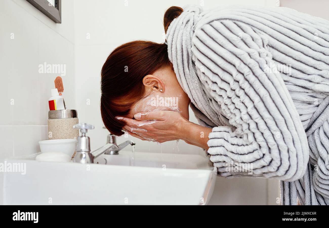 La mattina qui e il suo tempo di rinfrescarsi. Una donna irriconoscibile lavarsi il viso nel lavandino del bagno a casa. Foto Stock