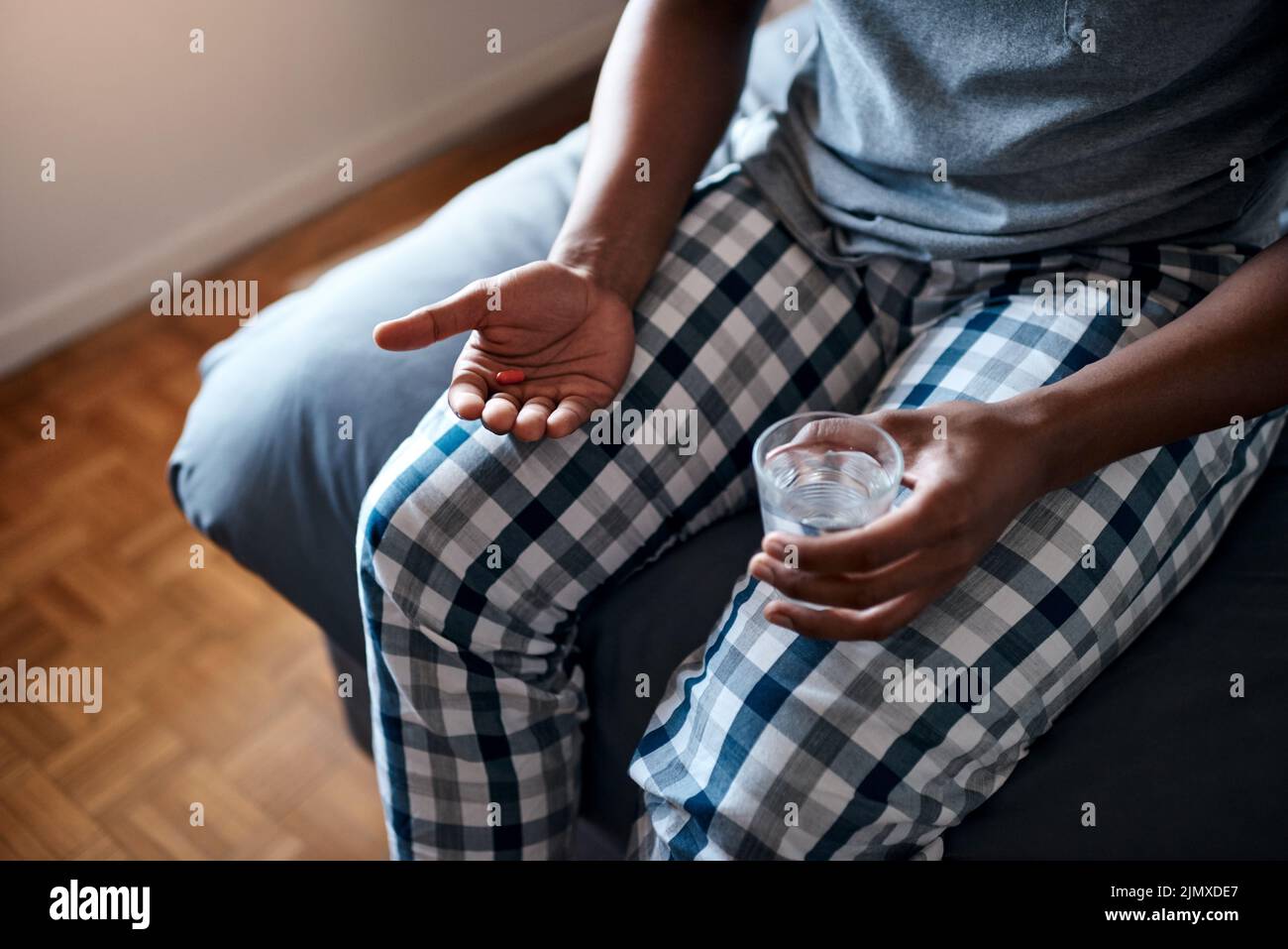 Spero che questi aiuti siano un uomo irriconoscibile seduto da solo sul letto e che prende antidolorifici con acqua. Foto Stock