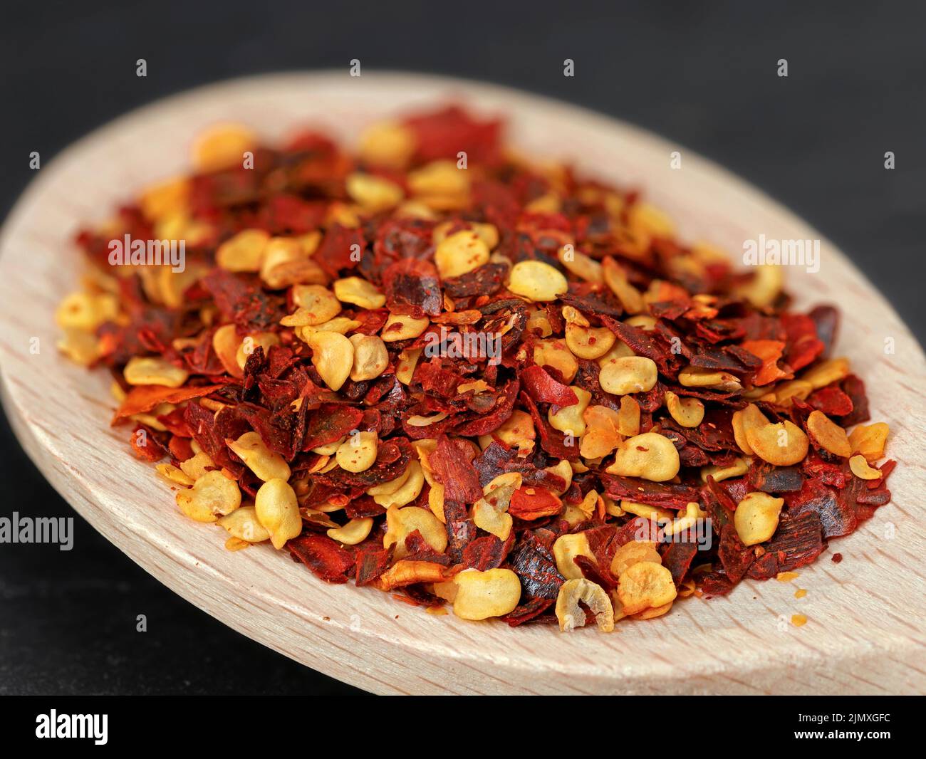 primo piano di scaglie di peperoni rossi in cucchiaio da cucina in legno, ingrediente caldo per cibi piccanti Foto Stock