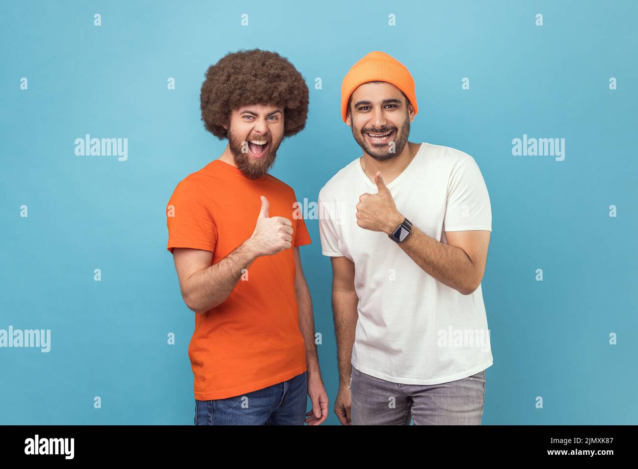 Ben fatto, ottimo lavoro. Due giovani uomini adulti che mostrano i pollici in su, gesturing gradiscono la macchina fotografica e sorridendo ampiamente, esprimendo l'approvazione, il feedback positivo. Studio interno girato isolato su sfondo blu. Foto Stock