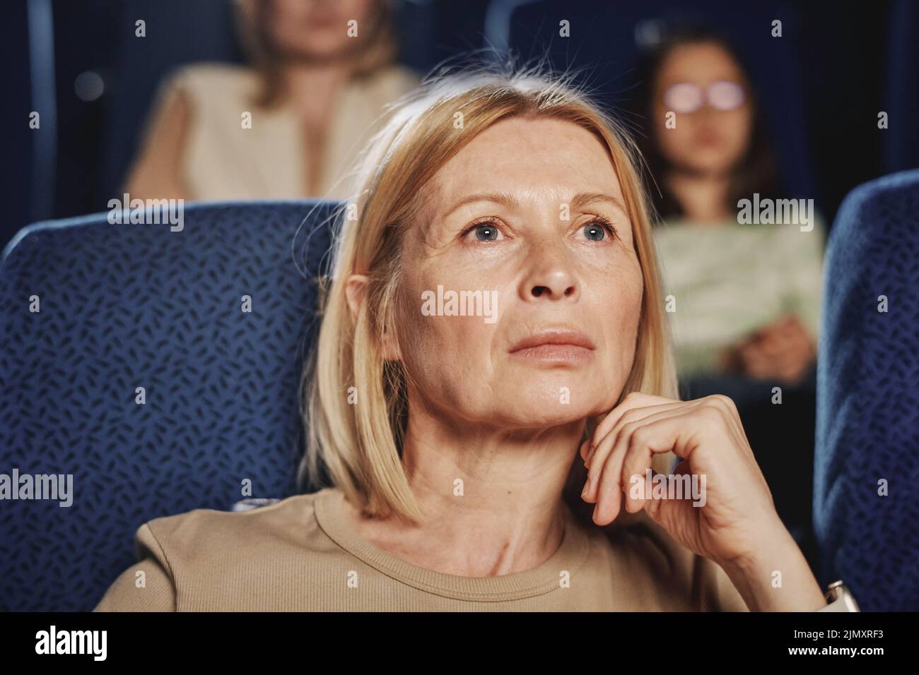Primo piano ritratto di matura donna caucasica con capelli biondi guardando film drammatico al cinema Foto Stock