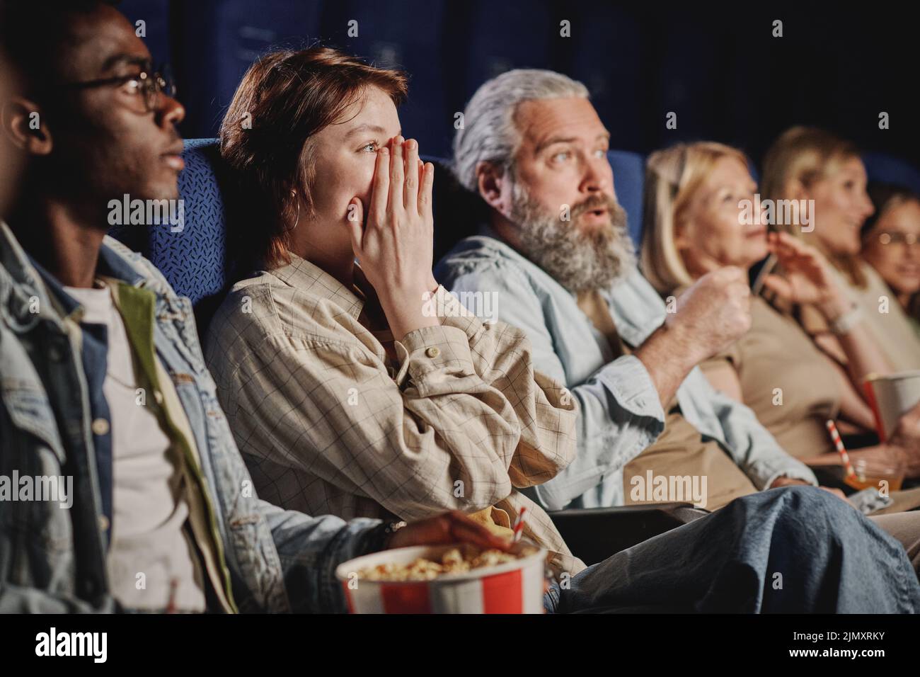 Un gruppo diversificato di persone che trascorrono la serata guardando un nuovo film al cinema reagendo alla scena Foto Stock