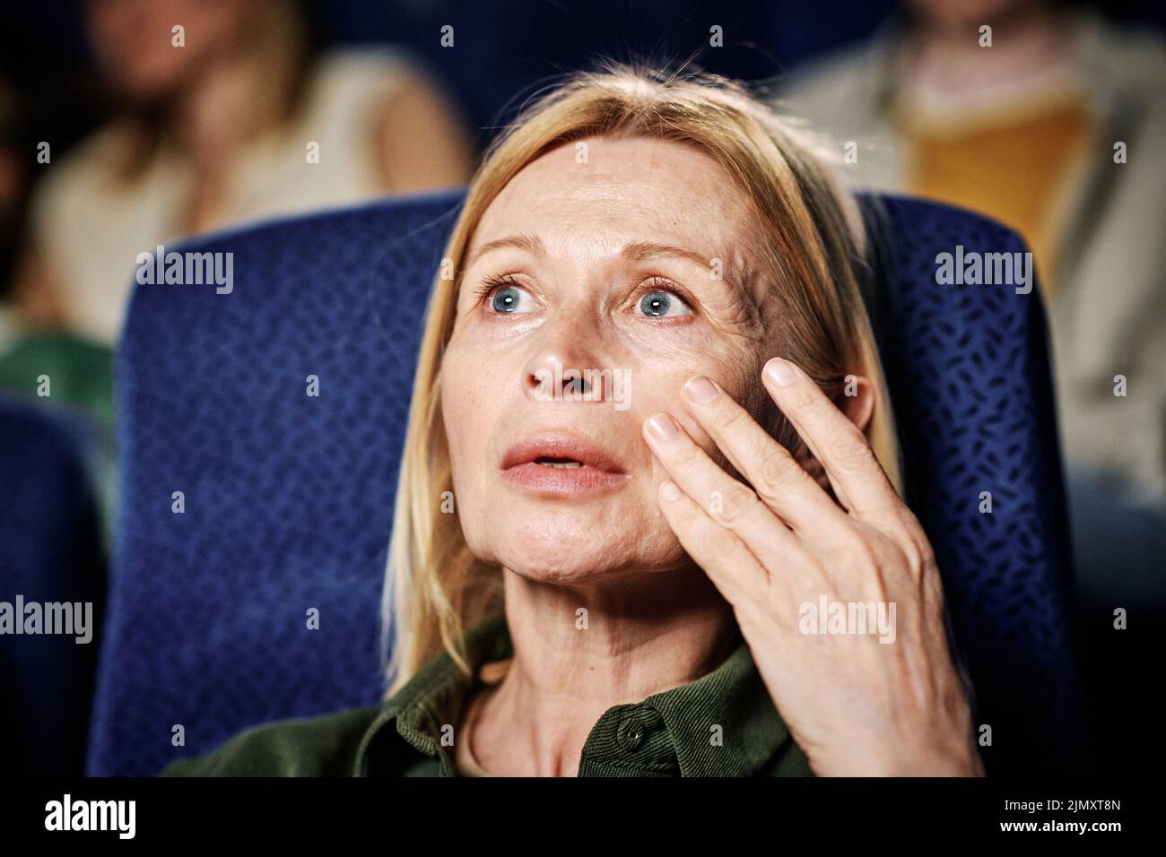 Primo piano ritratto di matura donna caucasica che diventa emotivo quando si guarda film drammatico al cinema Foto Stock