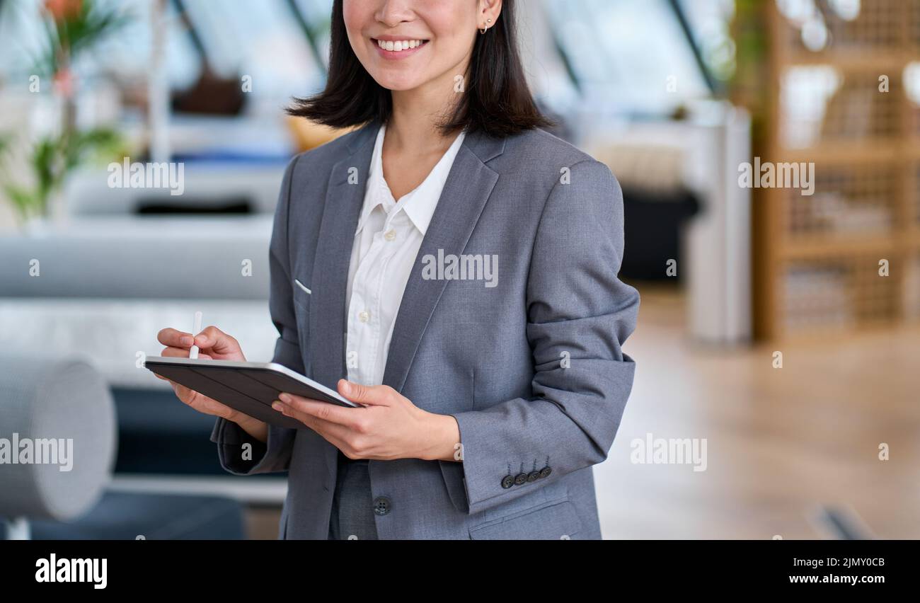 Giovane donna d'affari asiatica sorridente che usa un tablet digitale, primo piano. Foto Stock