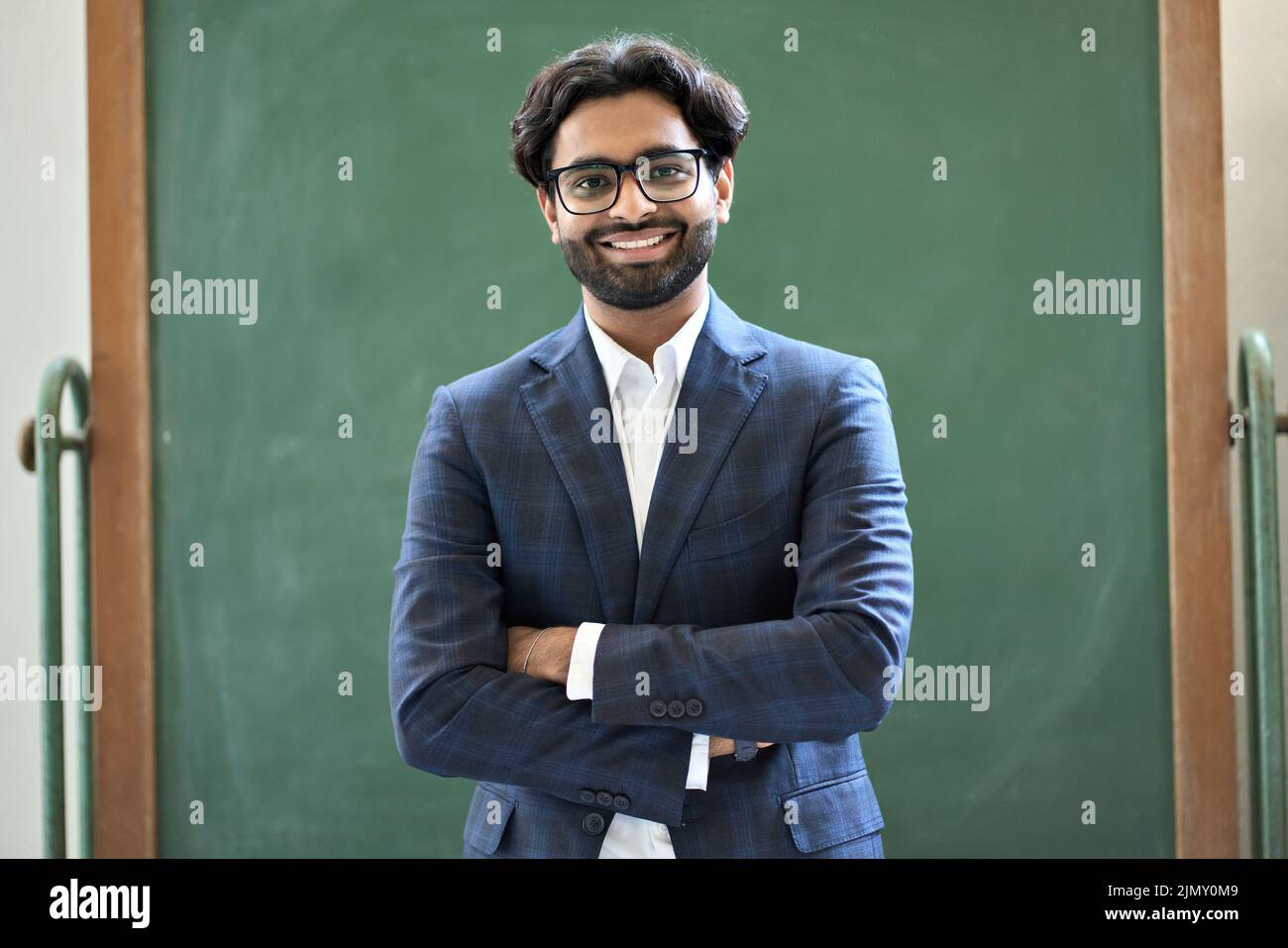 Sorridente uomo d'affari indiano che indossa un vestito in piedi in ufficio. Verticale Foto Stock