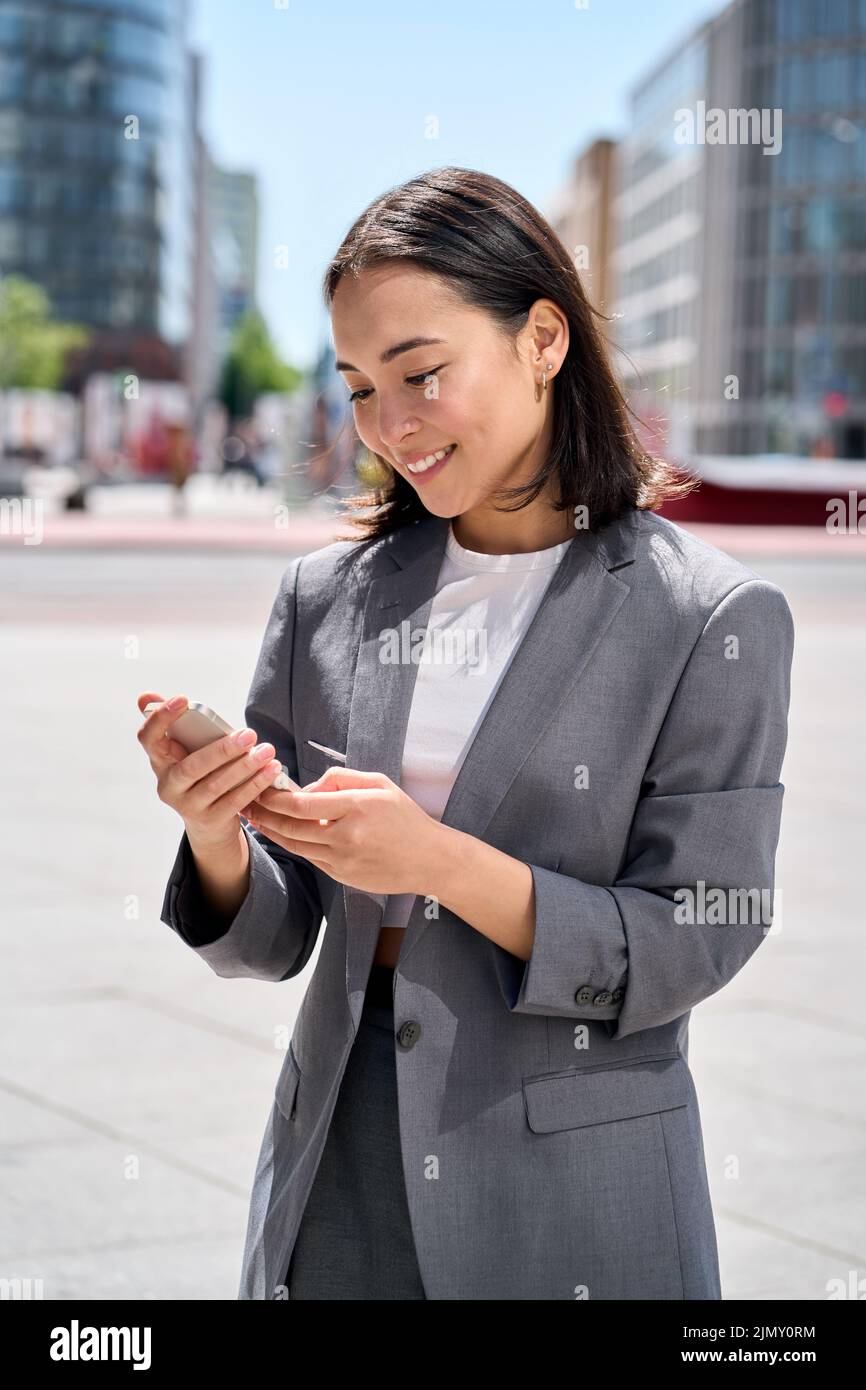 Giovane donna d'affari asiatica felice in piedi sulla strada della città usando lo smartphone. Foto Stock