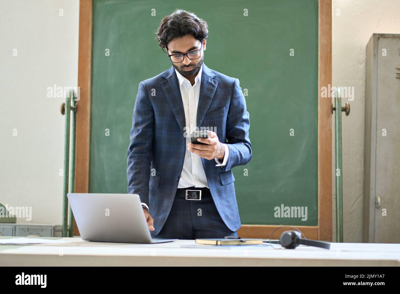 Giovane uomo d'affari indiano che usa il telefono che lavora sul laptop in ufficio. Foto Stock