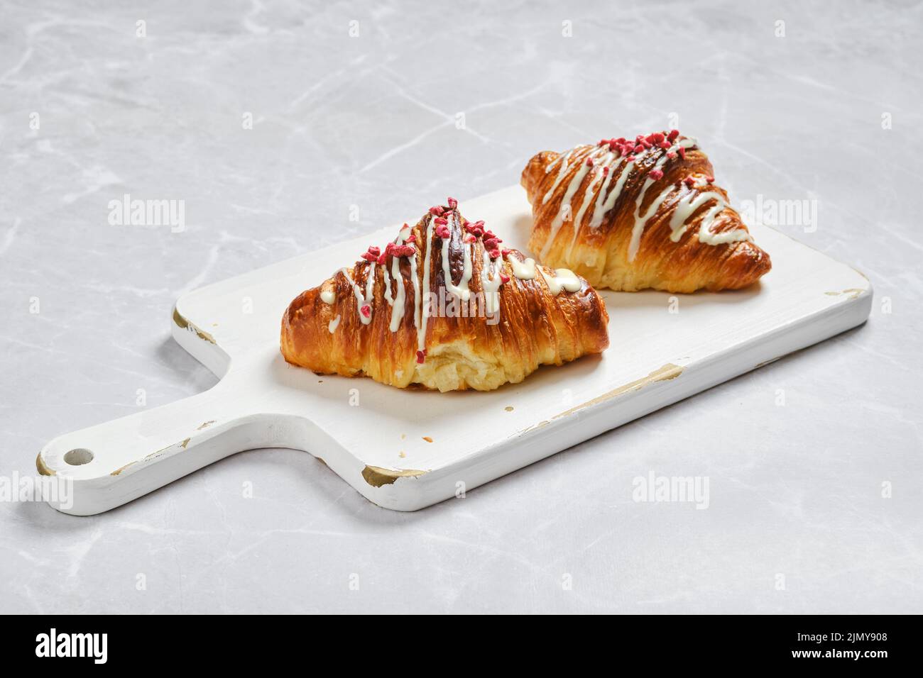 Due croissant con marmellata di lamponi su tavola bianca di legno su sfondo marmoreo Foto Stock