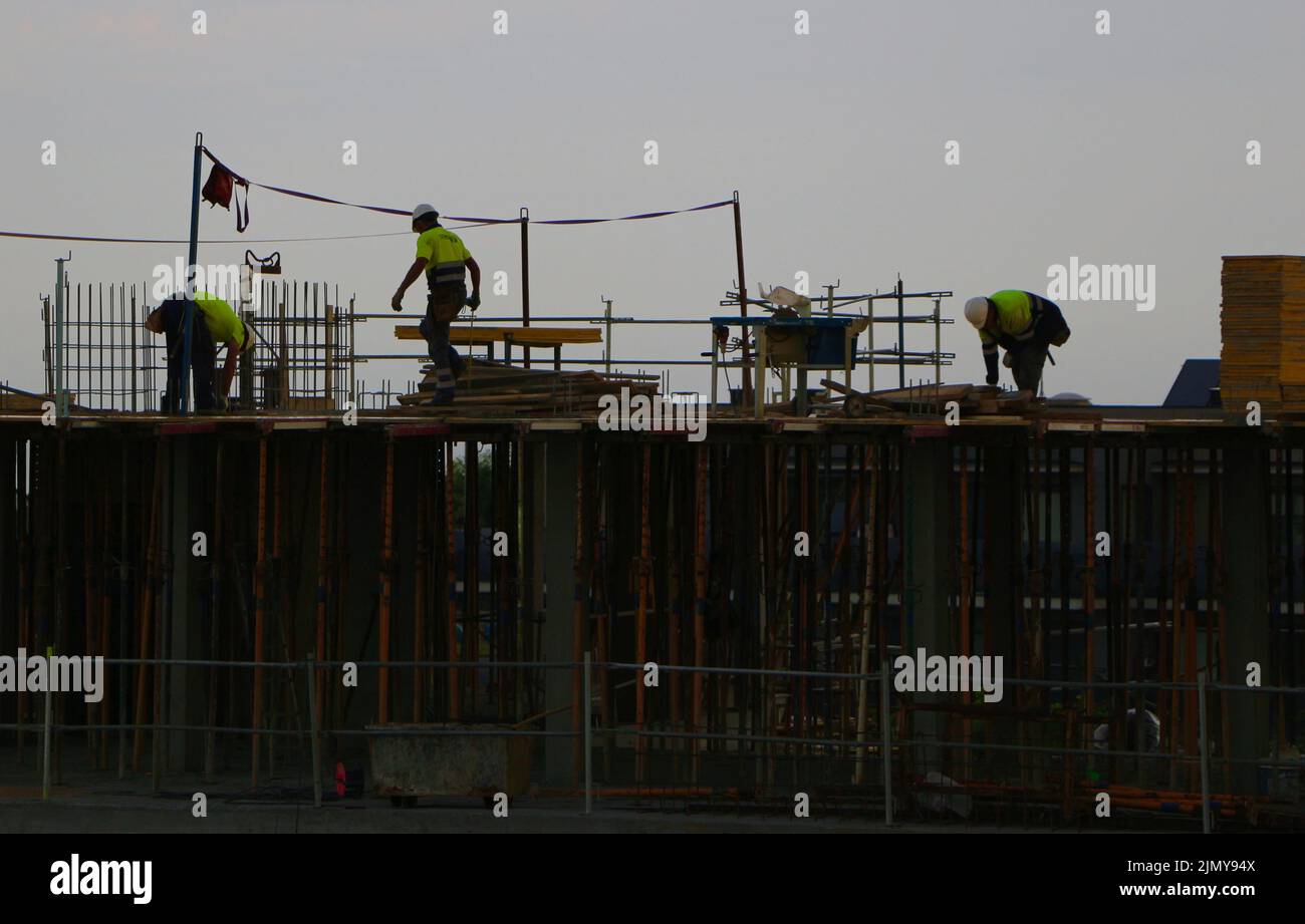 Lavoratori edili su un nuovo blocco di costruzione di appartamenti contro un cielo nuvoloso scuro in una mattina di inizio estate Santander Cantabria Spagna Foto Stock