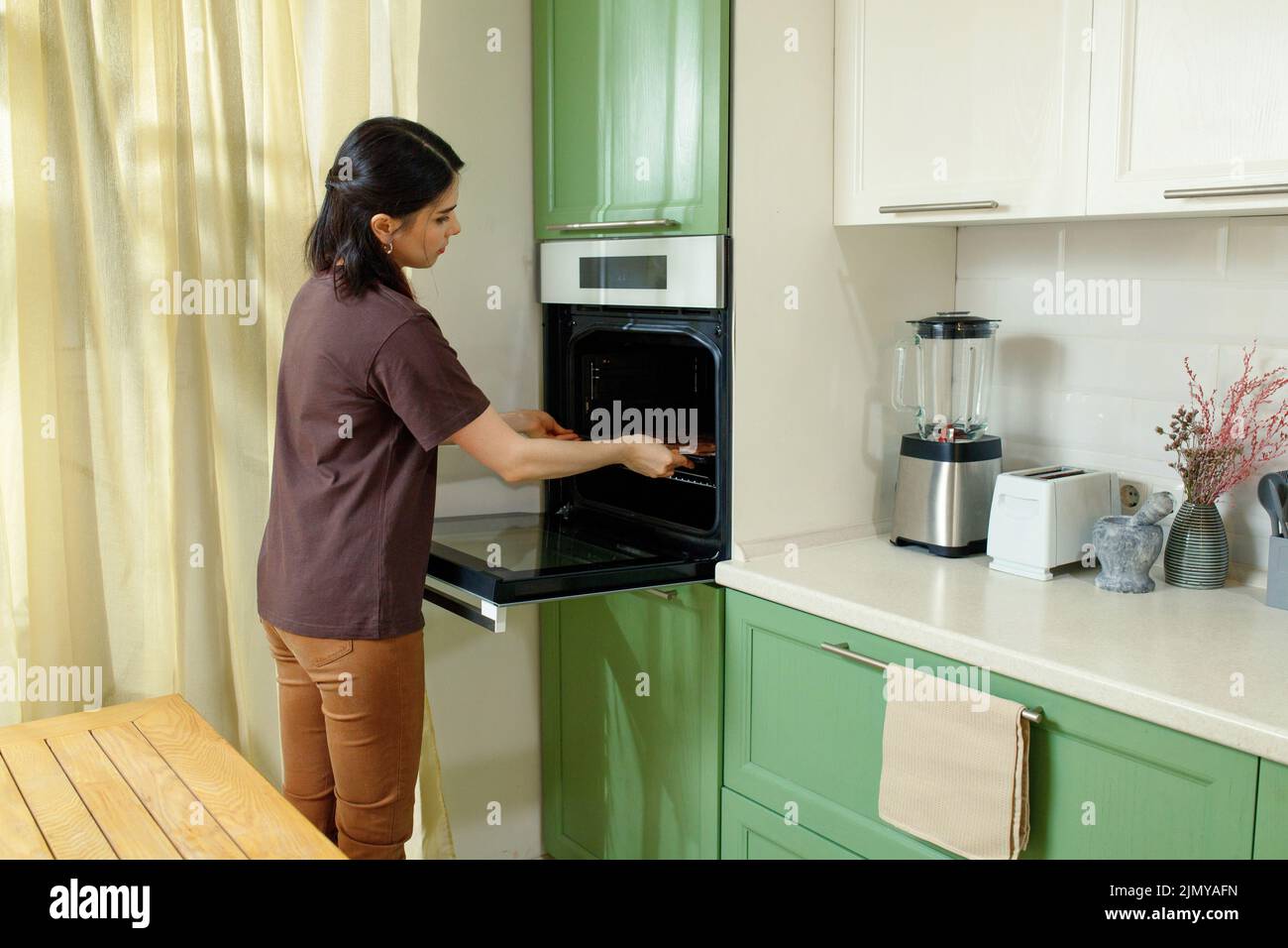 Una giovane donna si inforna in un forno che è ergonomicamente costruito all'interno al livello del petto Foto Stock
