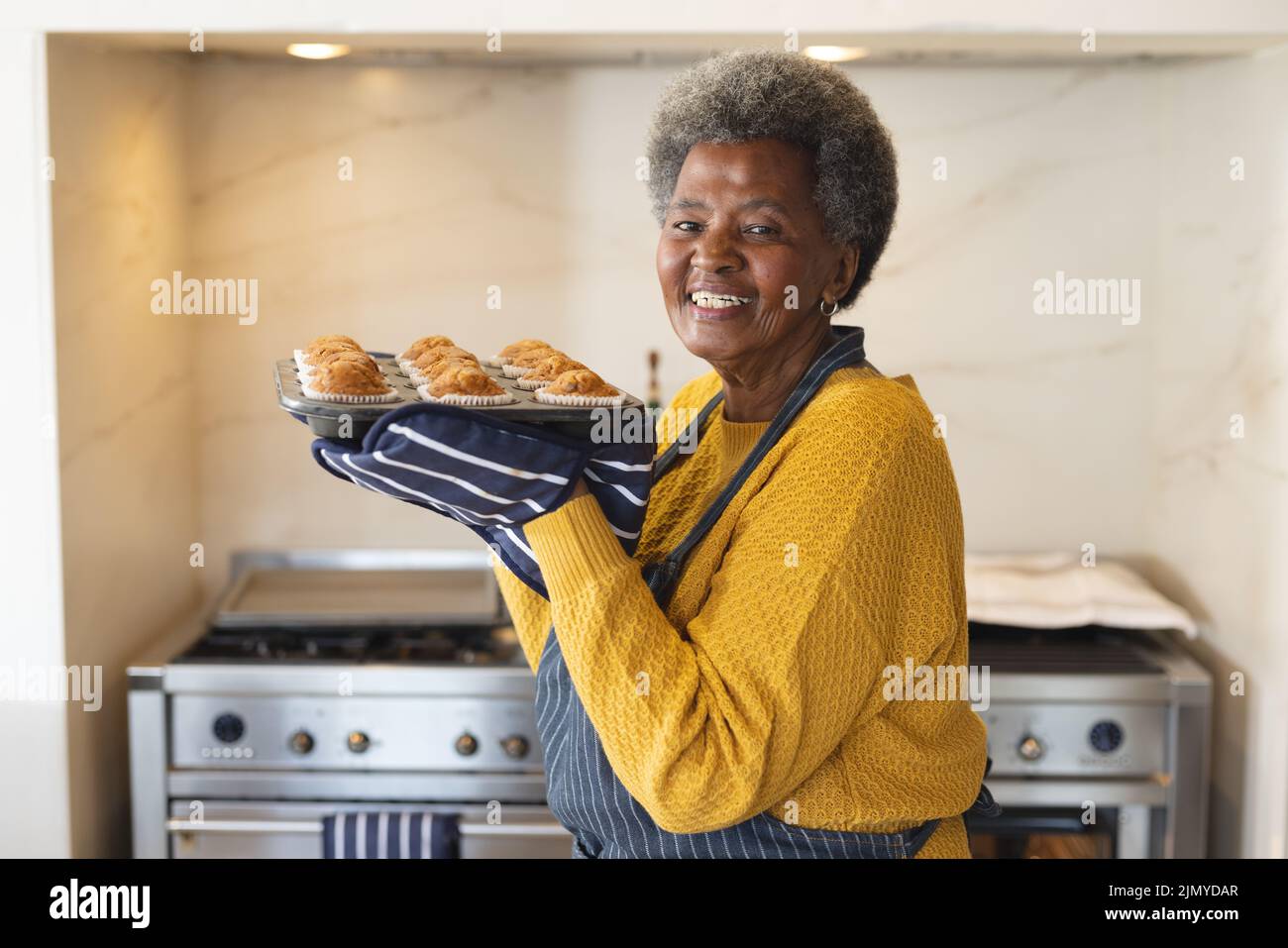 Immagine della donna anziana afro-americana felice con vassoio pieno di tortini appena sfornati Foto Stock