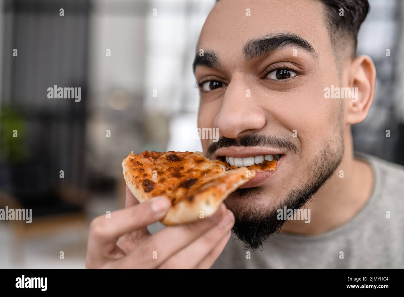 Faccia di uomo che guarda la macchina fotografica mordere la pizza Foto Stock