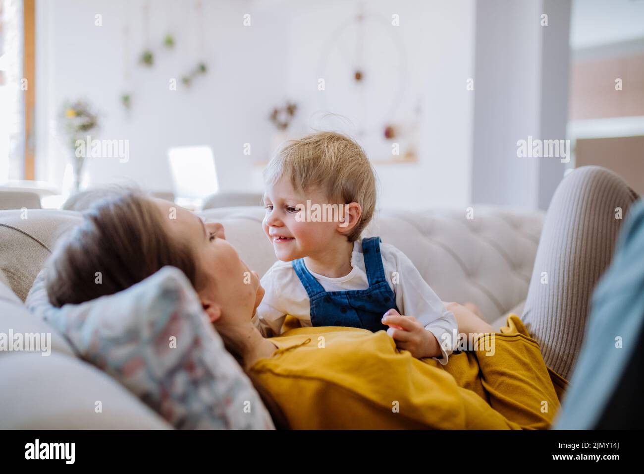 Giovane mamma allegra che gioca con il suo bambino e si diverte sul divano. Foto Stock