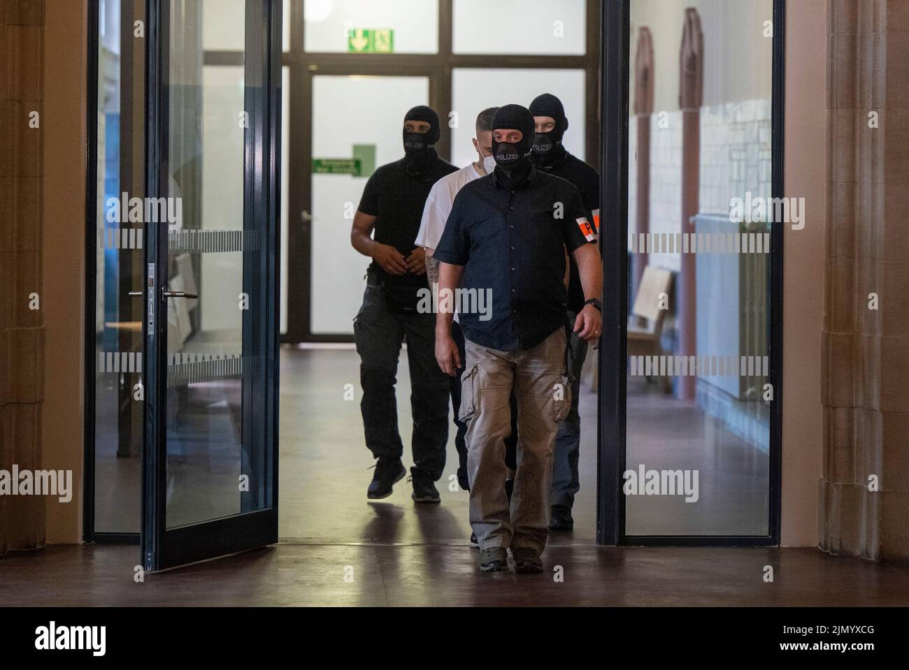 Berlino, Germania. 08th ago 2022. Anis Mohamed Youssef Ferchichi (centro, sotto copertura), noto con il suo nome di palcoscenico Bushido, entra in una sala di tribunale accompagnata da ufficiali di polizia all'inizio del processo del capo di un noto clan arabo e di tre suoi fratelli. Il capo del clan e i suoi fratelli sono in prova per, tra l'altro, esordizione rapina aggravata, privazione della libertà e pericoloso danno corporeo. Credit: Monika Skolimowska/dpa/Alamy Live News Foto Stock