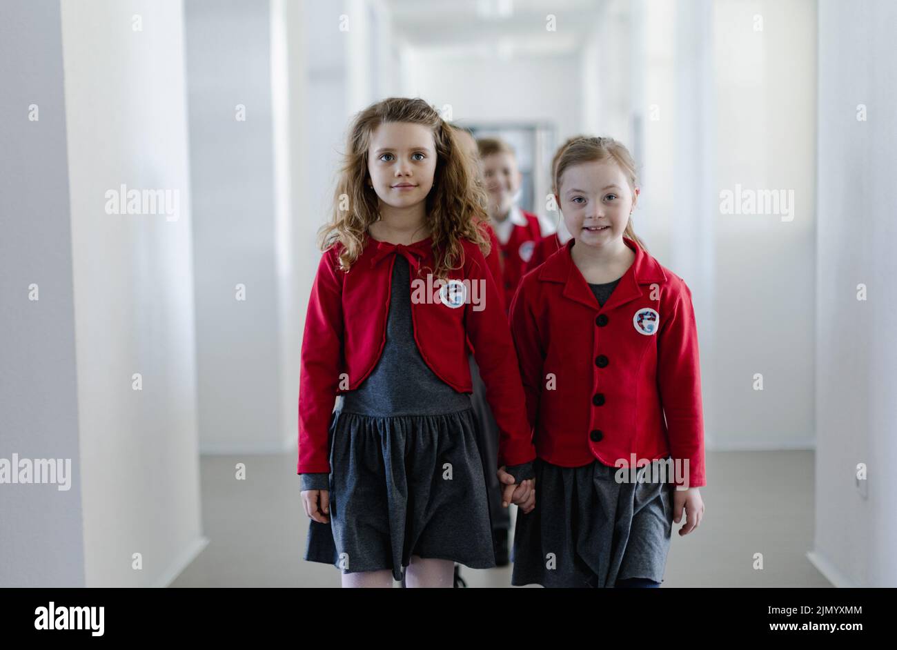 Felice schoolgrirl con sindrome di Down in uniforme a piedi nel corridoio della scuola con il suo compagno di classe, tenendo le mani l'un l'altro. Foto Stock