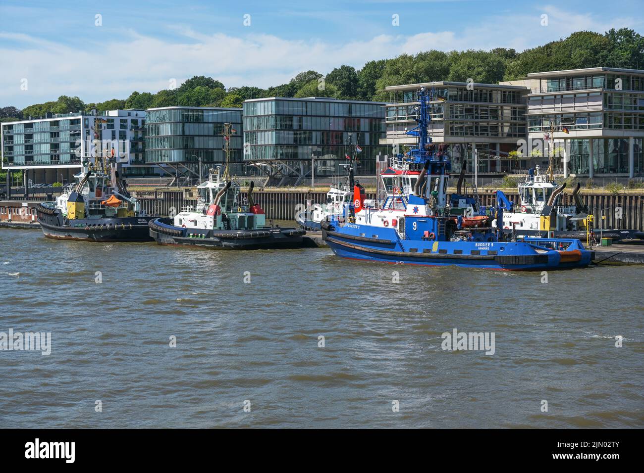 Amburgo, Germania, 3 agosto 2022: Rimorchiatori in fila nel porto di Amburgo di fronte agli edifici moderni, stanno trainando grandi navi e cargo a t. Foto Stock