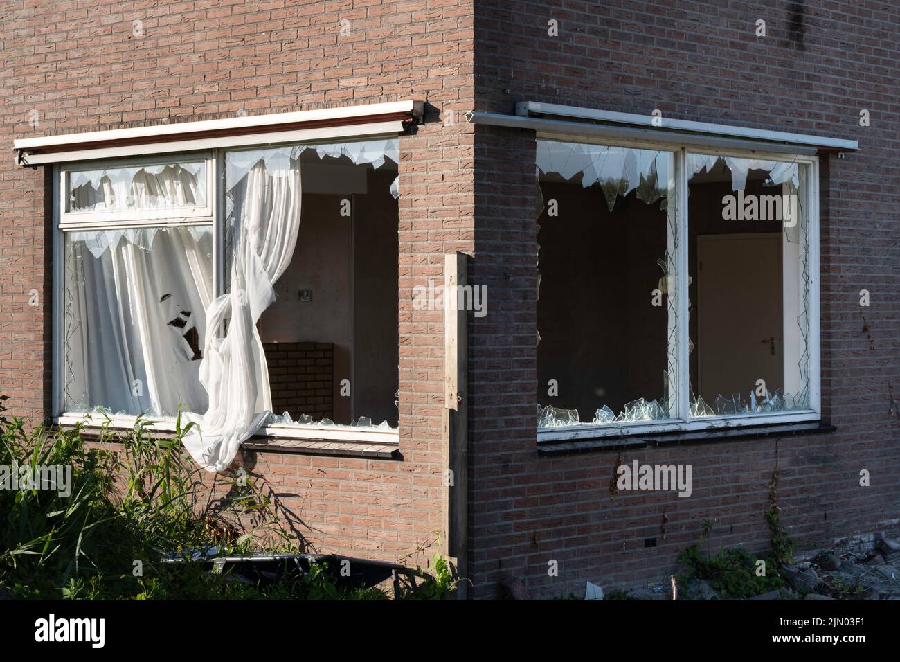 Finestre di vetro rotte, causate da vandalismo o demolizione, in un muro di mattoni di una casa, punti affilati di bastone di vetro dal rimborso. Tende che pendono fuori Foto Stock