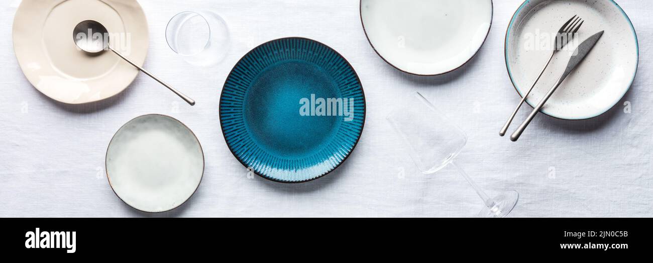 Moderno panorama da tavola con un piatto blu vibrante, posate, bicchieri, getto piano. Stoviglie alla moda su tovaglia Foto Stock