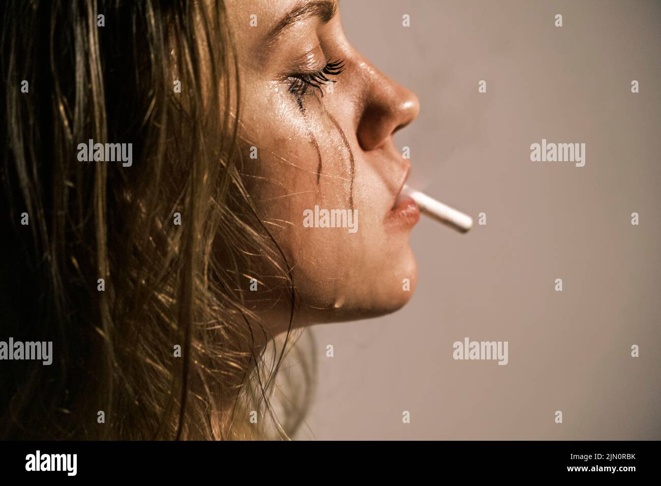 Piangendo la giovane donna con la sigaretta in bocca. Ritratto di vista laterale di donna infelice che sperimenta una crisi emotiva nella sua vita. Nazionale Foto Stock