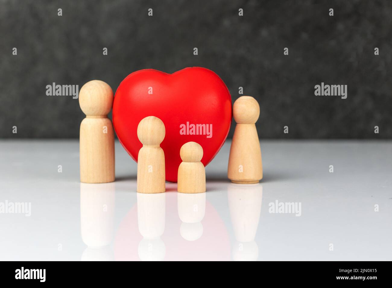 Quattro piccole figurine di legno che simboleggiano una famiglia - una madre, un padre e due bambini, vicino ad un grande cuore rosso. Il concetto di amore e cura della famiglia. Foto Stock