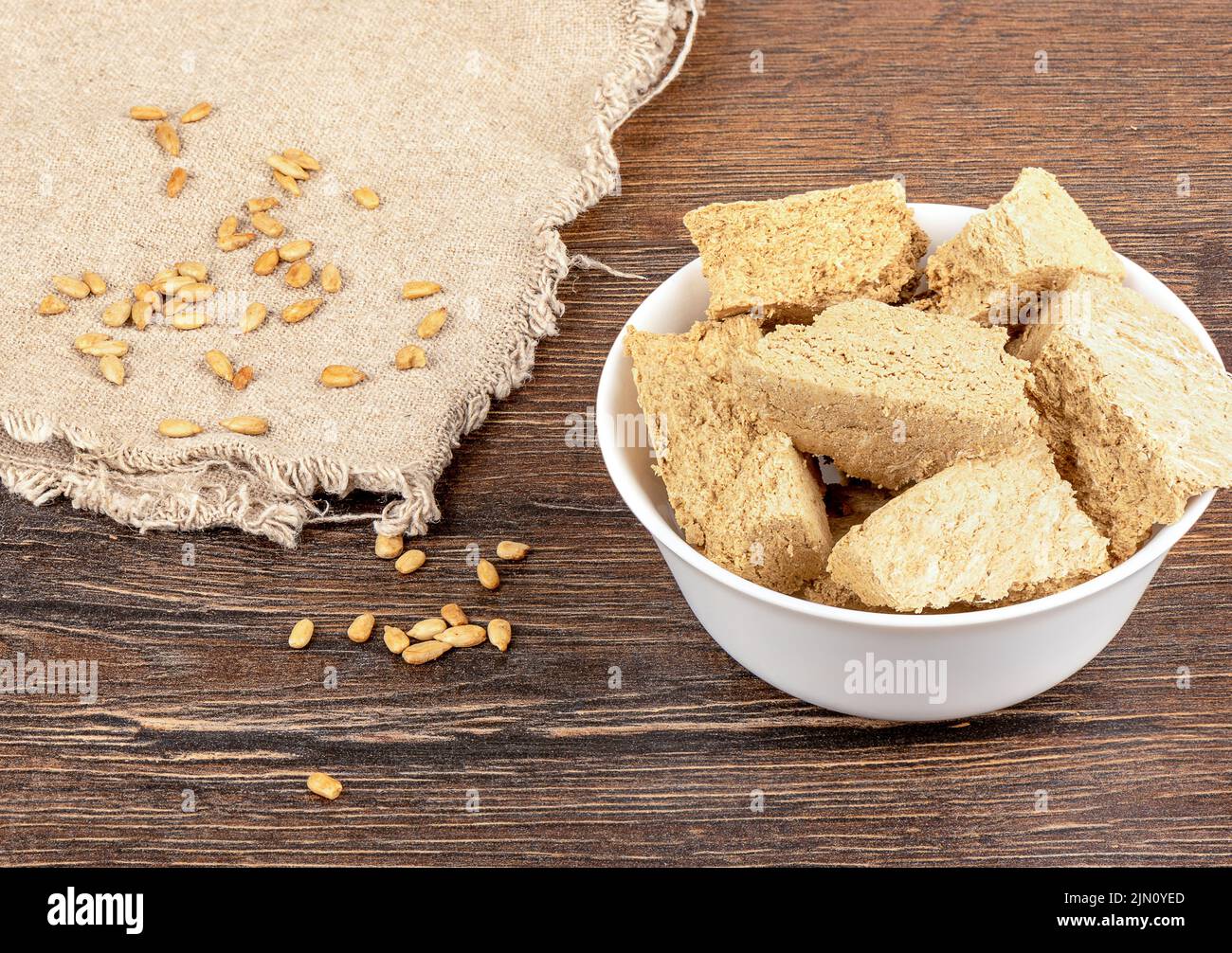 Semi di girasole su tela a grana grossa e halva di girasole tritata in una ciotola di porcellana bianca. Deliziosa halva di dolcezza orientale da semi di girasole. Foto Stock