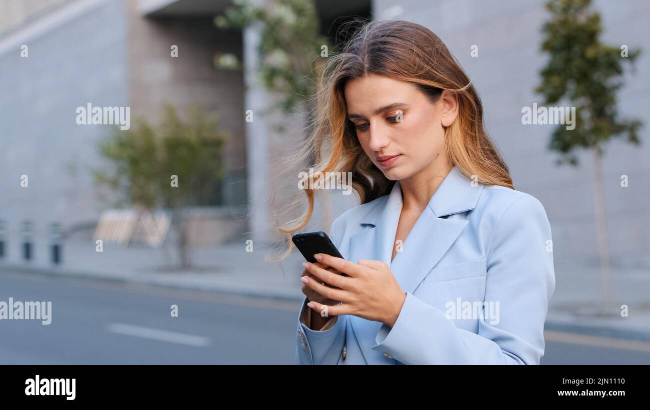 Primo piano ritratto in città bionda seria ragazza business donna utente si trova sulla strada guardando il telefono cellulare dispositivo wireless gadget utilizzando l'app per smartphone Foto Stock