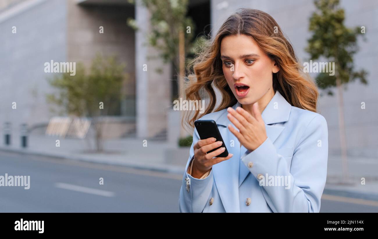Donna d'affari caucasica donna bionda donna all'aperto tenere il telefono cellulare leggere SMS spiacevoli notizie sentirsi indignant scioccato. Cattiva comunicazione da parte della banca Foto Stock