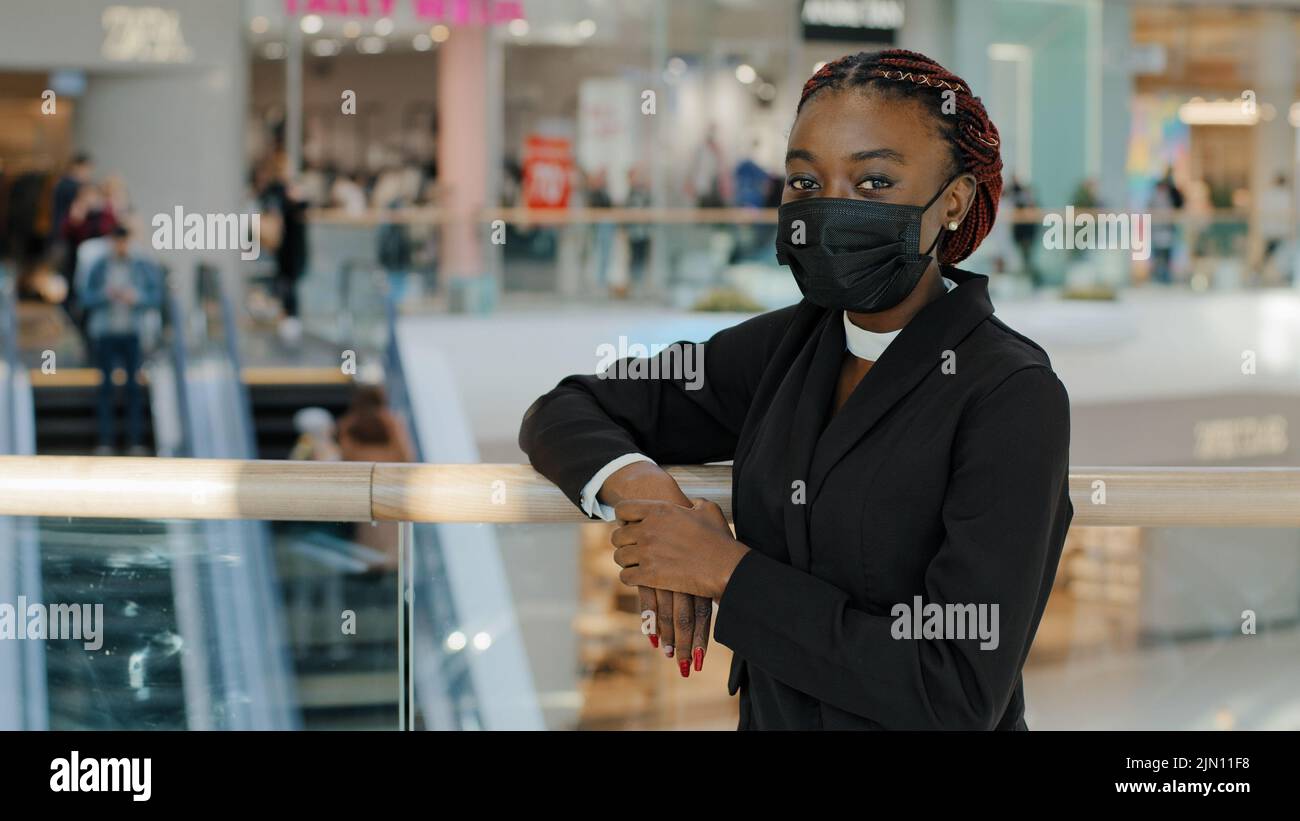 Ritratto di afro americano giovane ragazza donna acquirente consumatore indossa la maschera medica in piedi nel centro commerciale centro commerciale guardando la macchina fotografica in posa vicino ai negozi Foto Stock