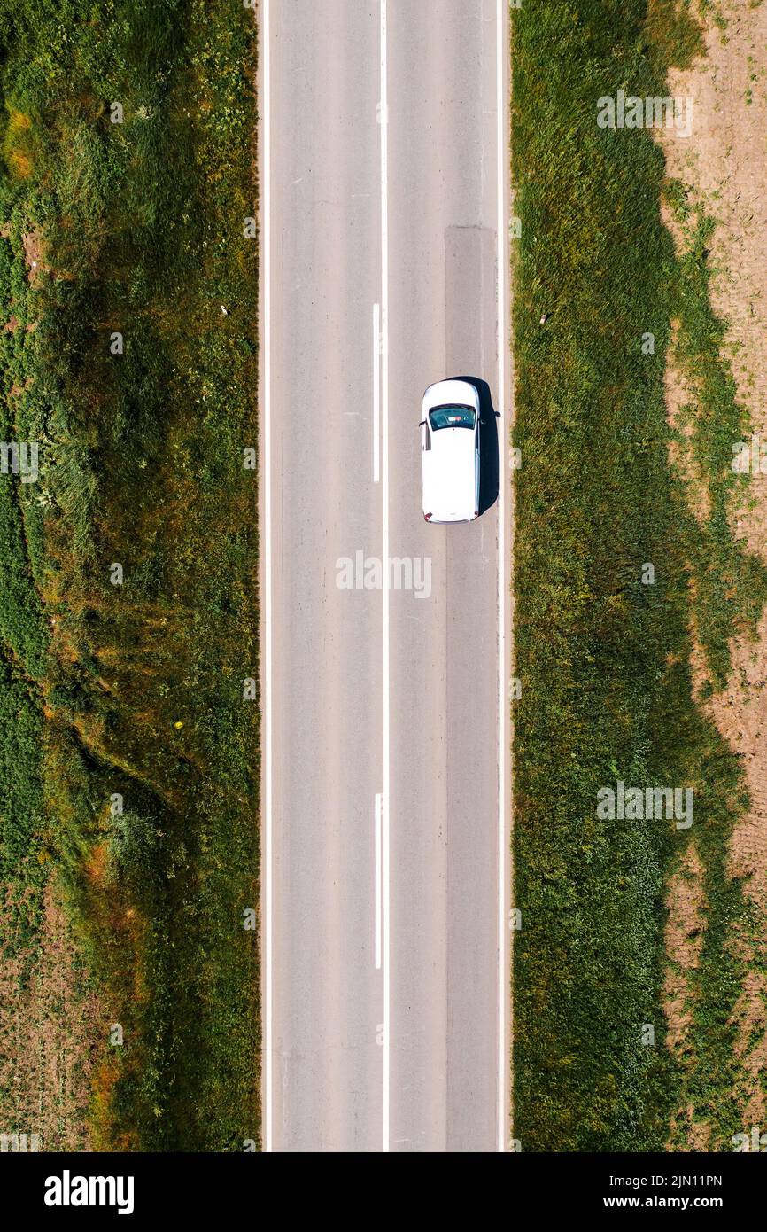 Il veicolo multiuso bianco guida lungo la strada attraverso il paesaggio di campagna nel caldo pomeriggio estivo, drone pov direttamente sopra Foto Stock