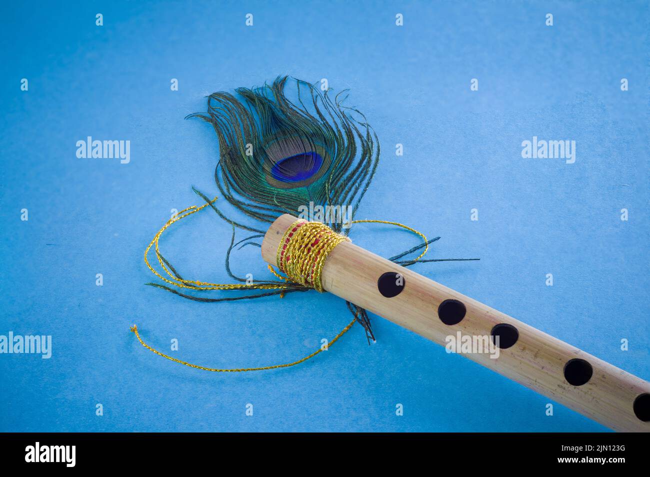 Flauto di bambù decorato con piume di pavone simbolico al dio indù lord krishna durante la celebrazione del festival janmashtami. Foto scattata in backgro blu Foto Stock