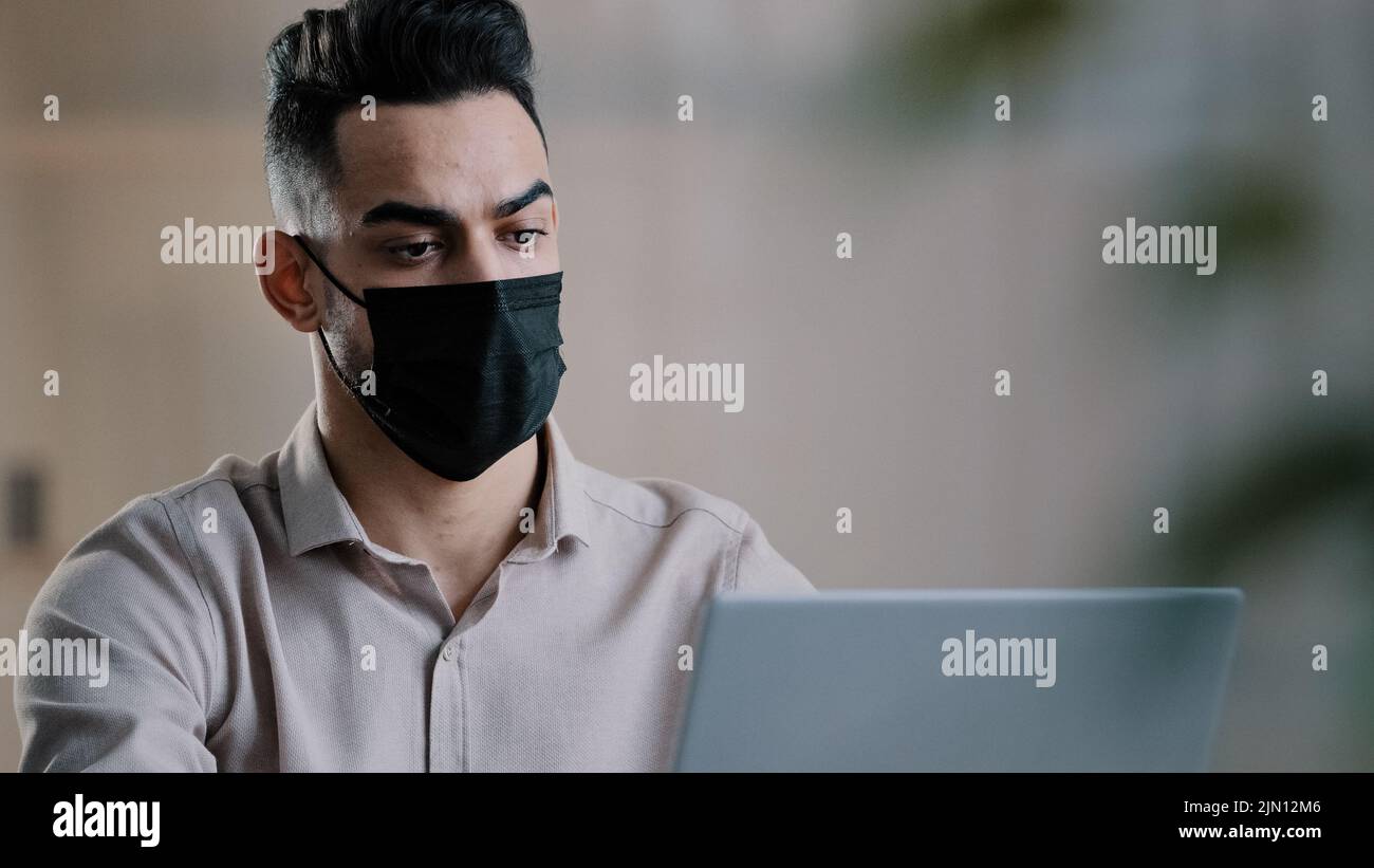 Arabian Sick uomo d'affari in maschera medica designer programmatore digitando su laptop di ricerca informazioni in rete sviluppare progetto di avvio chat in linea Foto Stock
