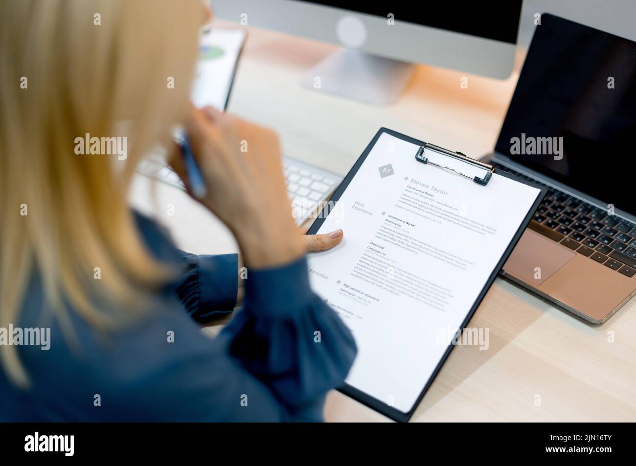 Reclutamento, colloquio di lavoro. La direttrice femminile dell'azienda, specialista di assunzioni in un'azienda, siede in una scrivania in un ufficio moderno, conduce un'intervista di assunzione, ha letto a fuoco il resume del candidato, prende una decisione Foto Stock