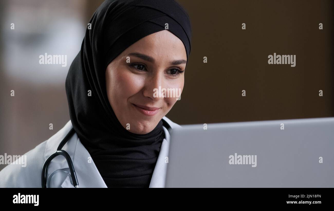 Sorridente ragazza ragazza chirurgo medico musulmana araba in hijab dare consultazione online per il paziente fornire assistenza remota in chat virtuale prendere Foto Stock