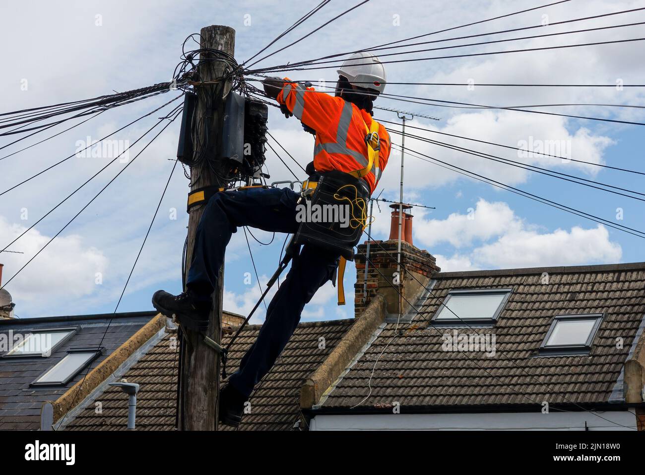 Tecnico delle telecomunicazioni che esegue la manutenzione sulla parte superiore di un palo del telefono. Foto Stock
