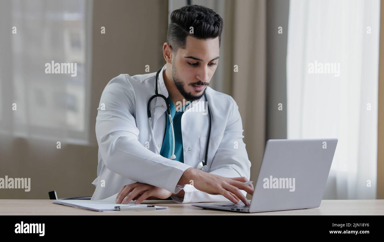 Uomo arabo concentrato medico professionista siediti al gabinetto clinica uso computer chatting distante in medico sociale app dare consultazione online Foto Stock