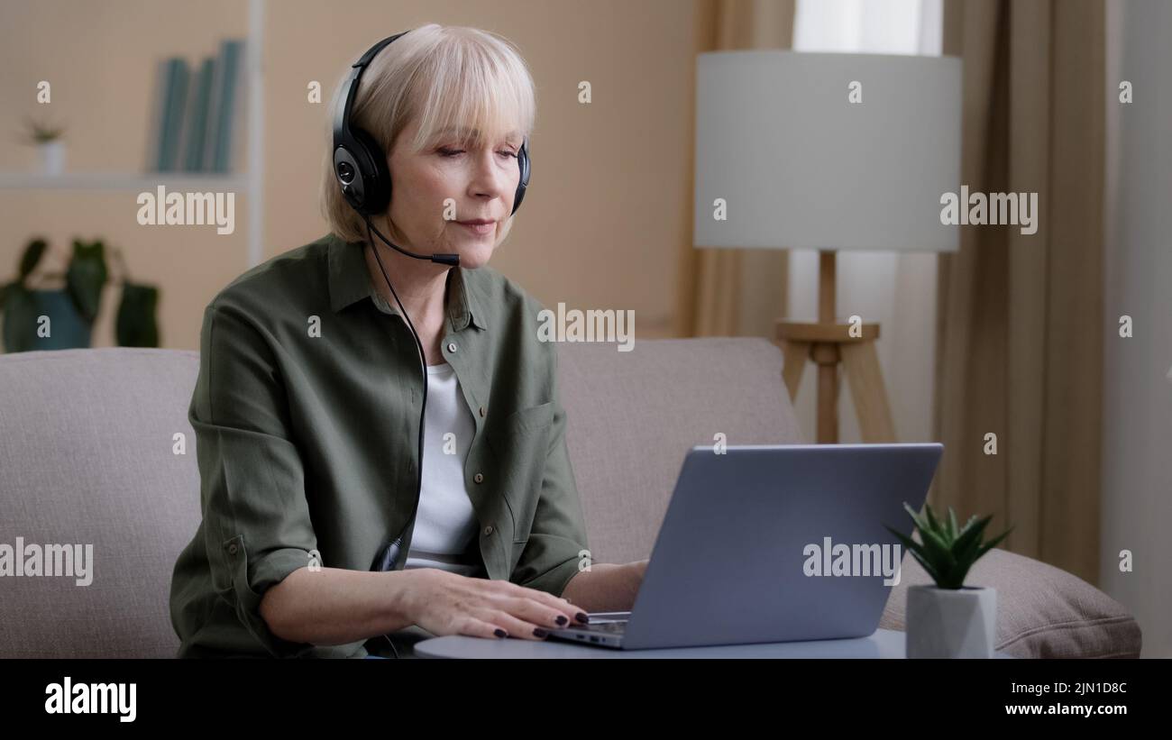 Donna d'affari di mezza età in cuffia che parla video conferenza a distanza riunione chiamate a distanza con il laptop. Vecchia insegnante caucasica anziana online femminile Foto Stock