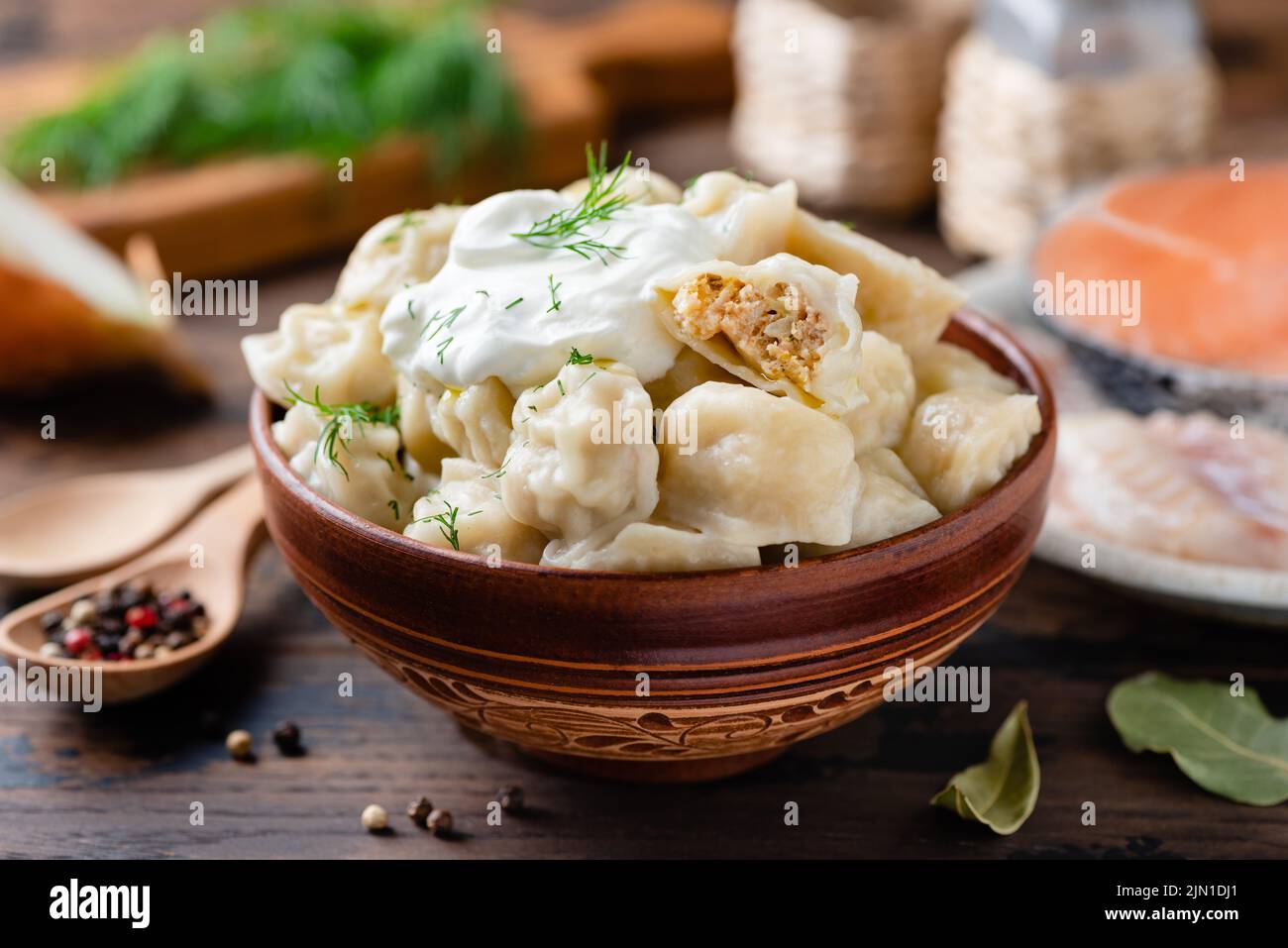 Gnocchi o pelmeni ripieni di pesce in una ciotola servita con panna acida e aneto, vista closeup. Cucina russa Foto Stock