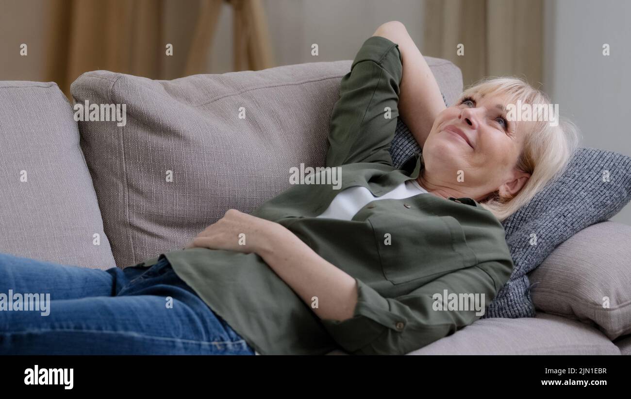 Felice rilassato di mezza età pene sognare donna riposo sul divano a casa godere di umore pacifico, sonnolento pigro calma anziano anziano anziano matura signora sogni sdraiati sopra Foto Stock