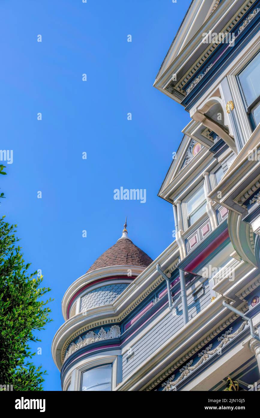 Vista ad angolo basso di una casa vittoriana con parete a torretta contro il cielo limpido a San Francisco, CA. Home esterno con fregio decorativo e capesante Foto Stock