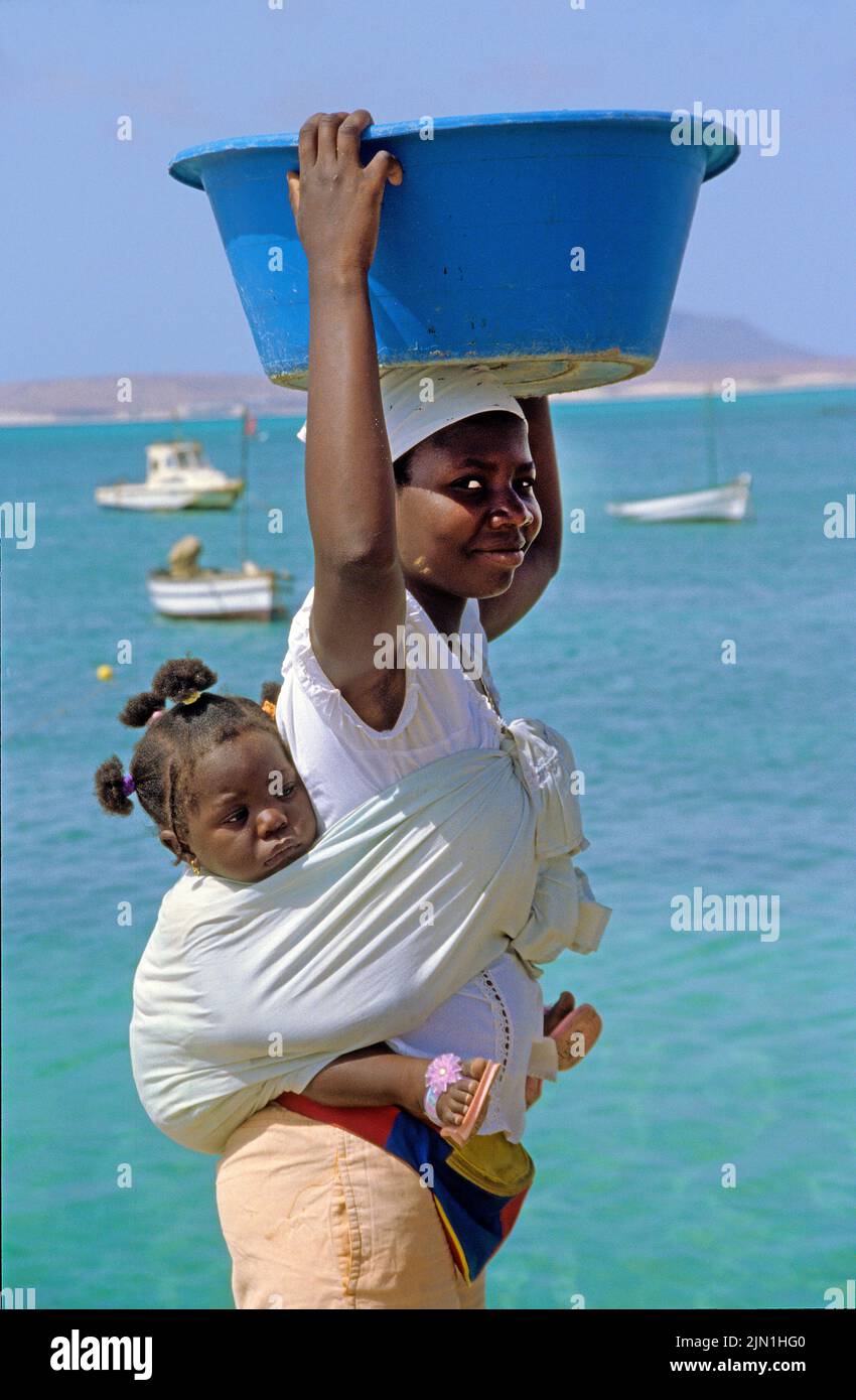 Donna locale che porta un bambino sul retro e un washbowl sulla testa, SAL Rei, Boavista, Isole di Capo Verde, Africa Foto Stock