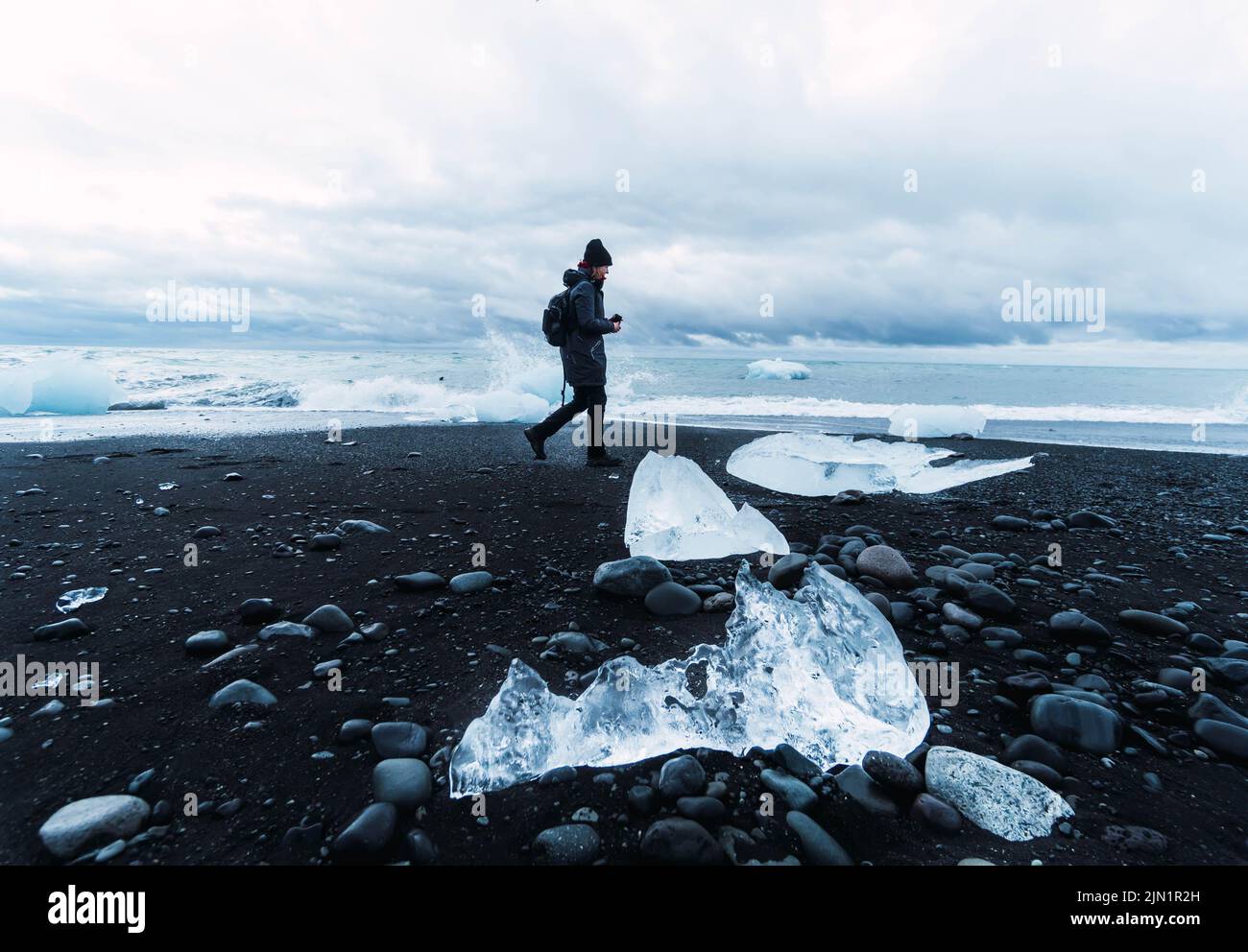 persona sulla spiaggia nera circondata da pezzi di ghiaccio Foto Stock
