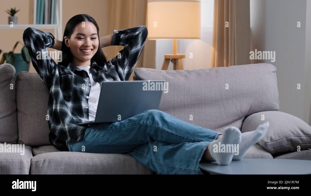 Donna asiatica ragazza coreana studente freelance donna utente seduta sul divano con le mani dietro testa riposo lavoro pausa stop e-learning guardare film online Foto Stock