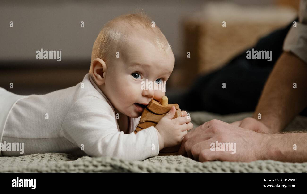 Famiglia caucasica irriconoscibile padre papà giocare con bambina figlio neonato bambino neonato bambino sdraiato a casa sul pavimento con giocattoli cuccioli di legno Foto Stock